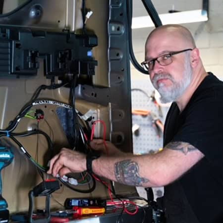 Ein Mann mit Brille und Bart, konzentriert bei der Arbeit an elektrischen Kabeln.